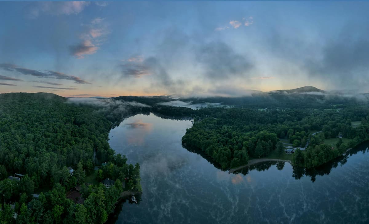Misty lake at sunrise framed by forested hills
